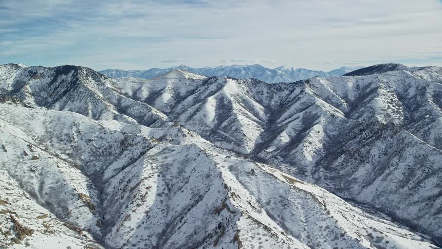 Aerial landscape of snowcovered mountain range on a blue sky day with clouds