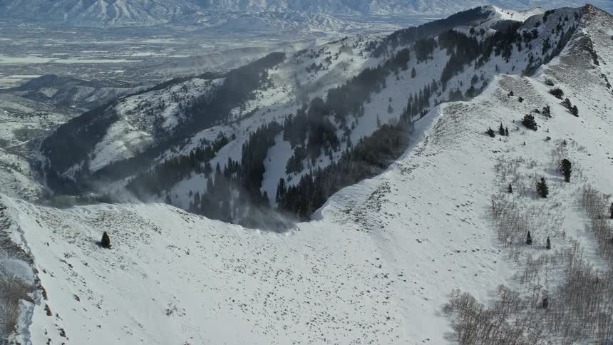 Aerial of snow drifting into air from mountain ridge in winter