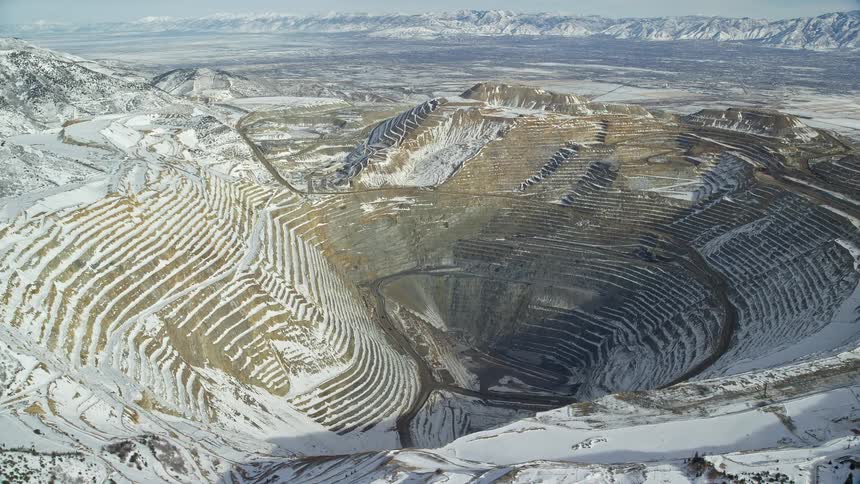 Aerial of brigham canyon mine with snow on a sunny day and pale white snowy peaks and sky in the background