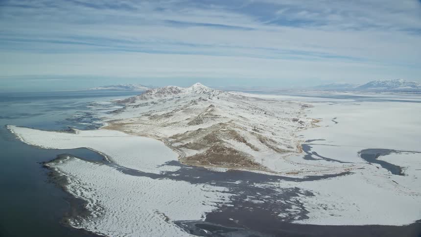An island with a hill surrounded by the ocean with snow covering it