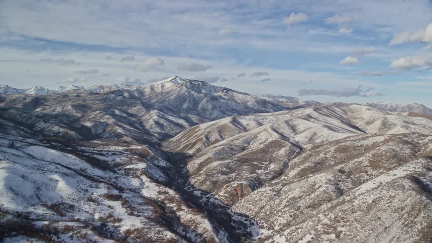 Snow dusted rocky mountain peaks in the sun under a bright blue sky with thin clouds