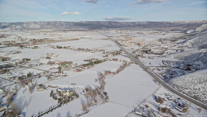 Aerial panorama of a road passing through mountains a river and an urban city covered in snow