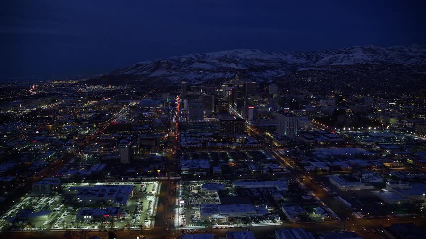 A city at night with the house lights on and a snowcovered mountain in the background