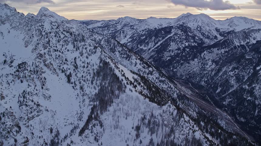 Aerial of valley in mountain range covered in snow and woods during winter