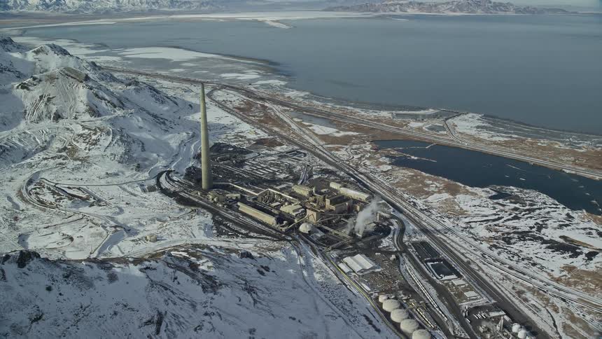 A factory at the base of a snowy mountain and close to a sea