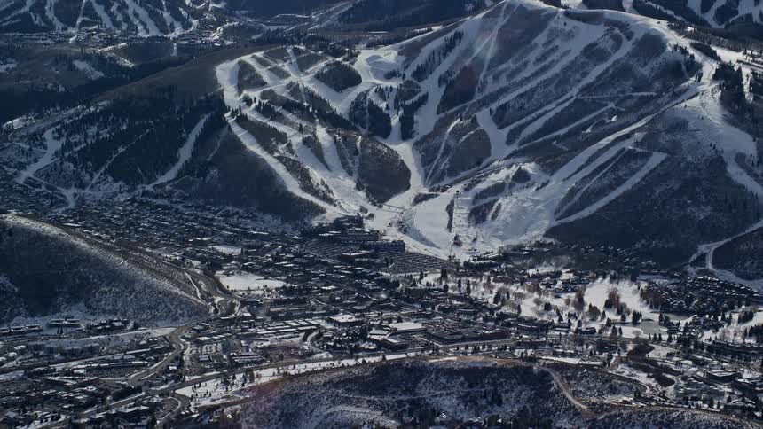 Aerial of snowy utah mountain with ski slopes and resort at the bottom on a sunny day
