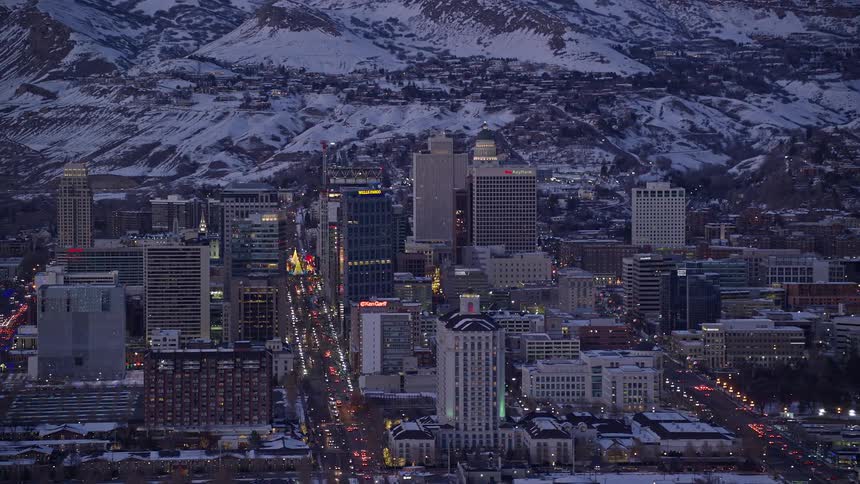 A city with huge buildings and vehicle traffic on a sunset and there is a mountain full of snow in the background