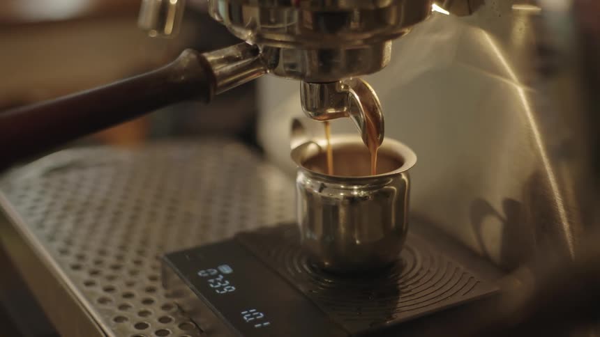 A machine is dispensing coffee into a metal cup on a scale at a shop