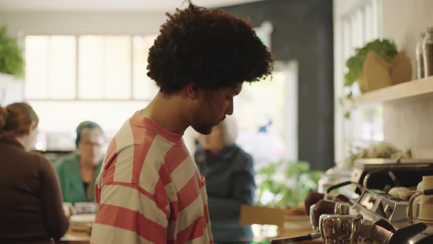 A man standing is making coffee and puts a cup on the table