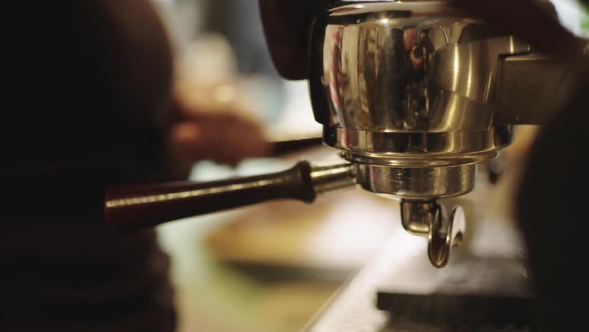 Closeup of a coffee machine with a hand adjusting the knob and placing a small cup for cappuccino