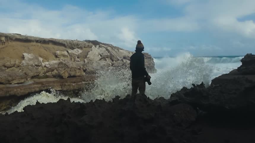Photographer stands near the crashing waves in the coast