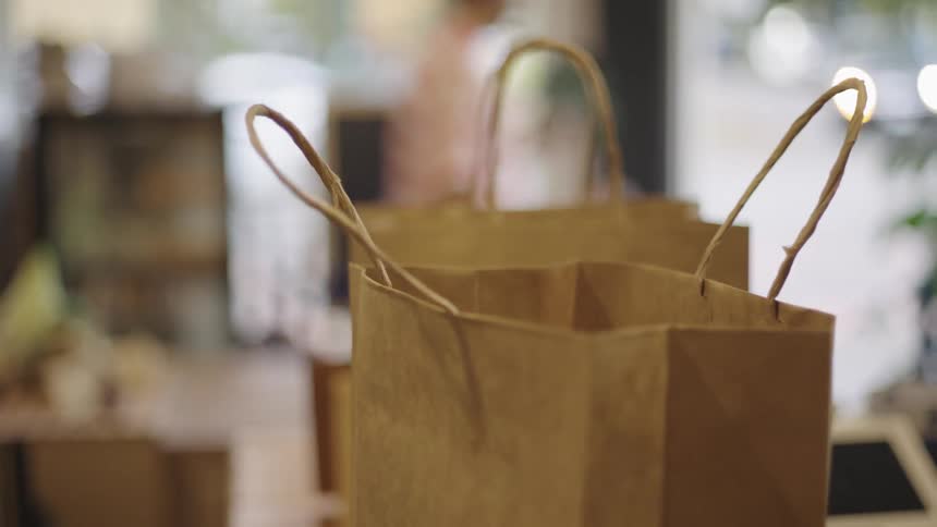 Closeup of a persons hands placing a paper box into a paper shopping bag with handles with blurred background in a retail environment