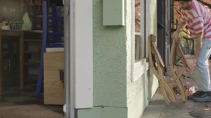 A man leaves a place and takes wooden chairs that are outside the establishment
