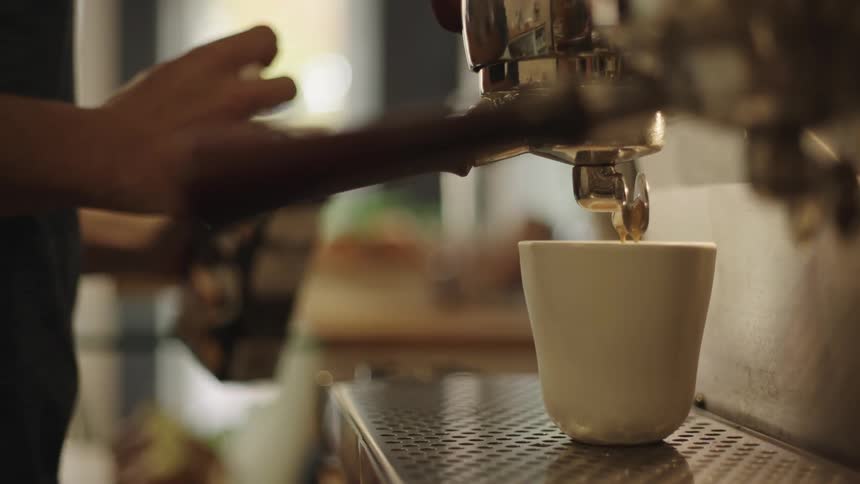 A machine that is pouring coffee into a stationary cup
