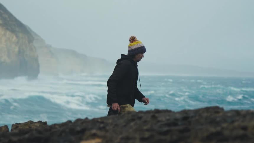 A man holding a camera walking by the beach side during the day