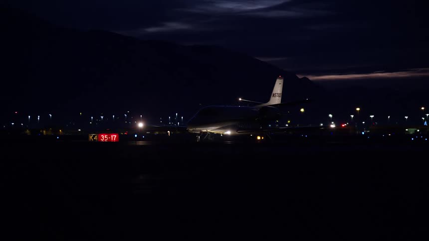 An airplane rolls down the runway with a lit up city and mountain behind it
