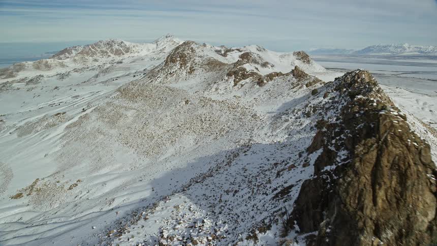 Aerial over jagged rocky snow dusted mountain ridge with blue sky on a sunny day
