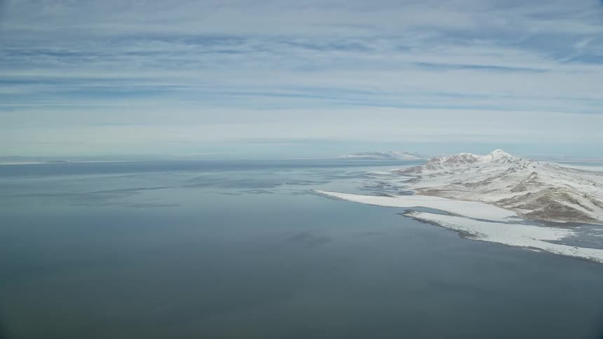 Aerial panorama of snowcovered ground next to a sea and a chain of mountains on the horizon