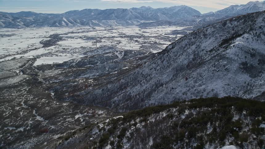 Aerial of a snow dusted valley between two mountain slopes shadowed with sunlight and mountains in the background