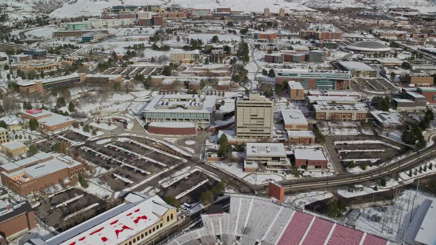 Aerial view of an urban city with a stadium in the center covered in snow and a chain of mountains on the horizon