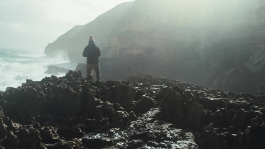 A person on the shore of a rock on the sea coast during the day