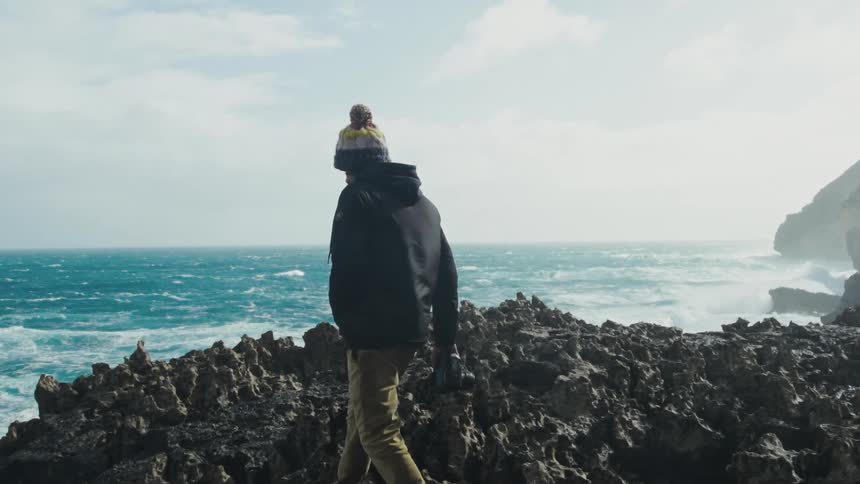 Photographer walks over the rocks next to the ocean