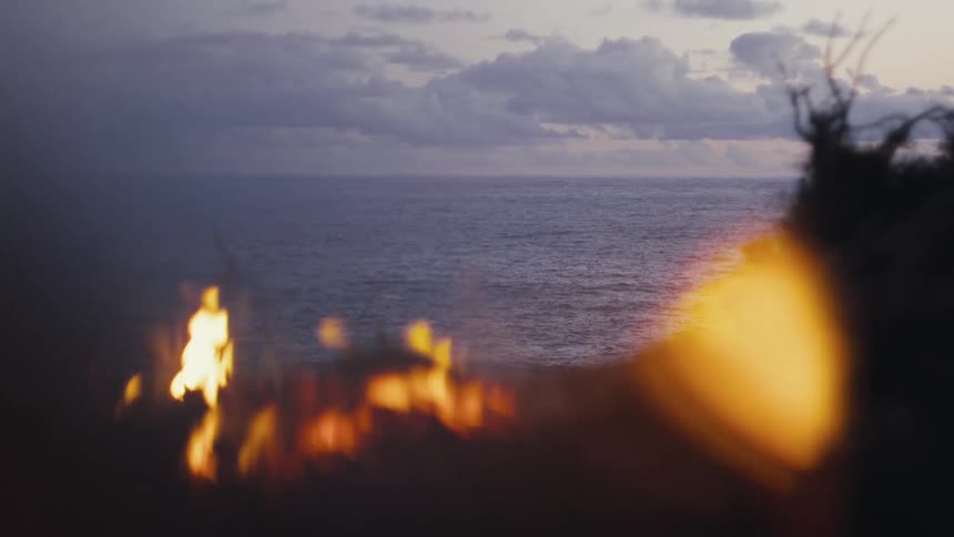 A bonfire in the meadow with the ocean in the background during sunset