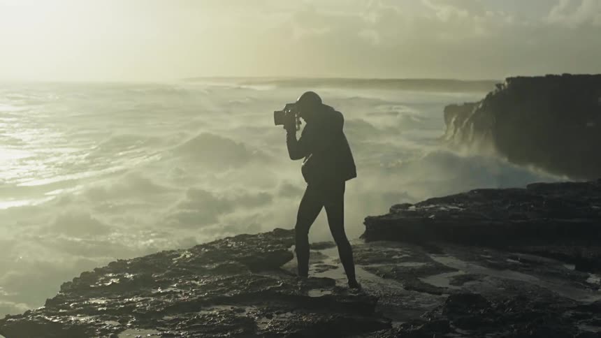 Photographer on the edge of a cliff taking pictures of the strong sea with the sunrise