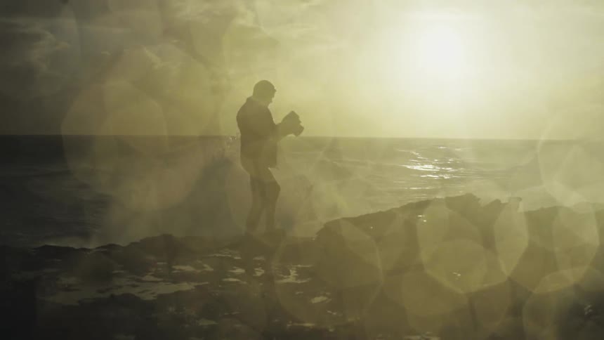 Photographer on a cliff by the coast with foamy waves on a sunny morning