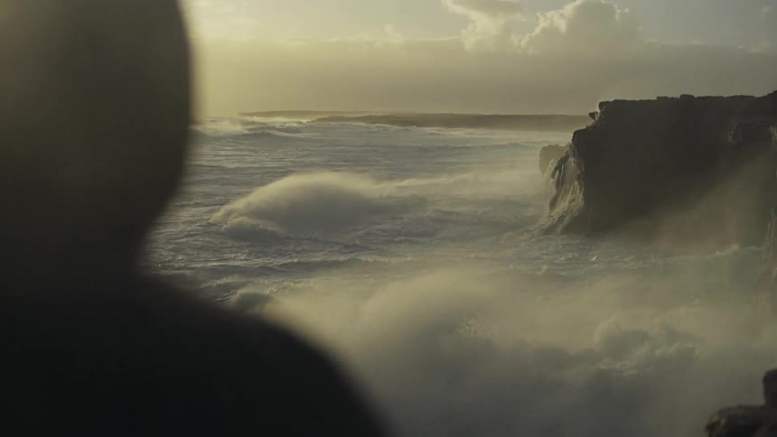 The waves crash against the rocks on the shore