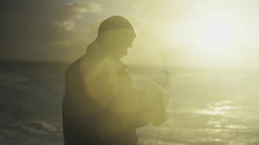 Man holding a camera next to the sea with sunlight beneath him