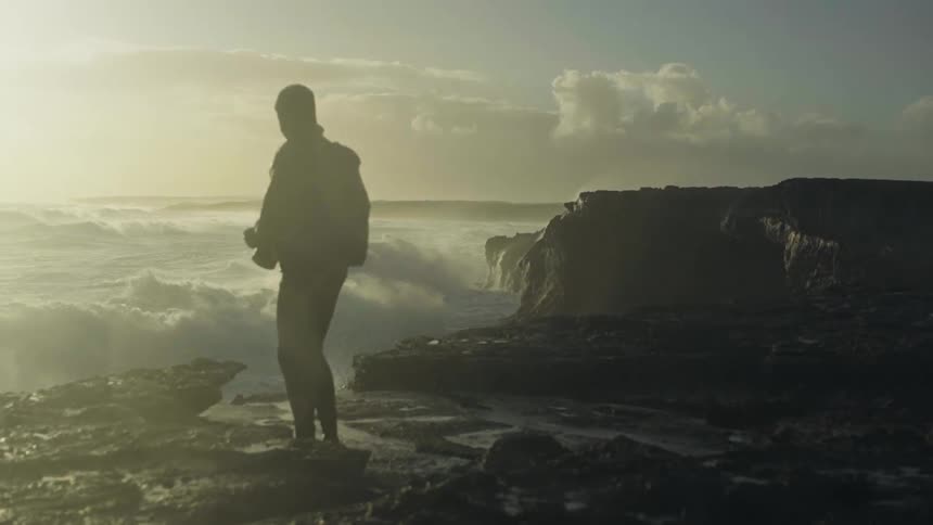 A man photographing the sea waves crashing on the rocky mountain shore