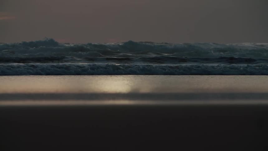 Ocean waves breaking against the sandy beach at sunset