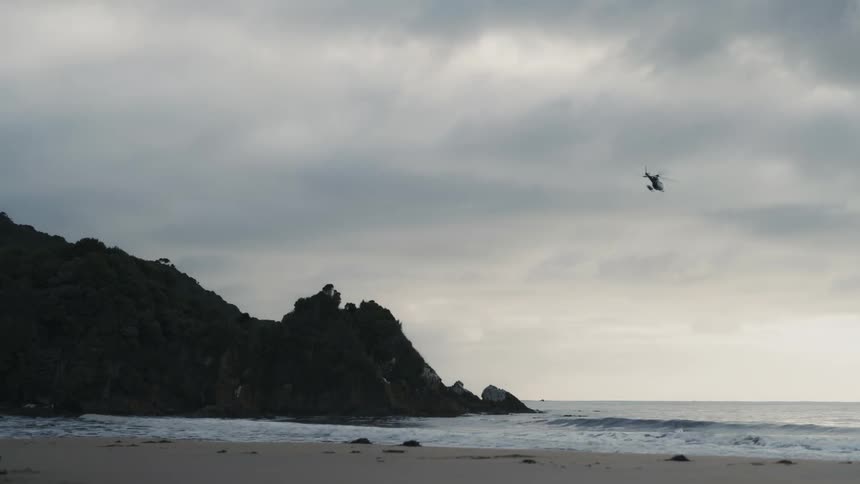 A helicopter flying over a deserted beach during sunset