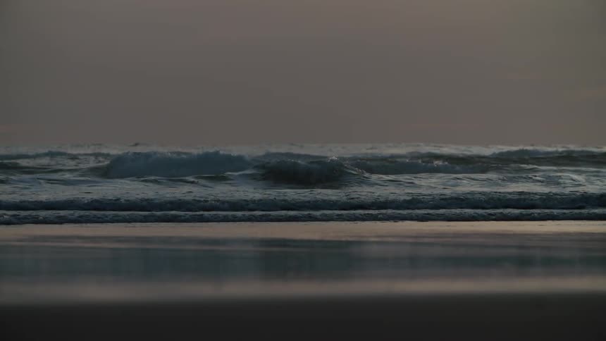 Sea waves crash onto the beach during sunset
