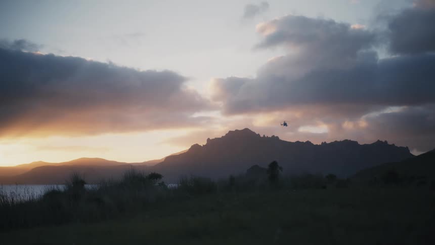 A helicopter flying over the landscape of fields and mountains during sunset