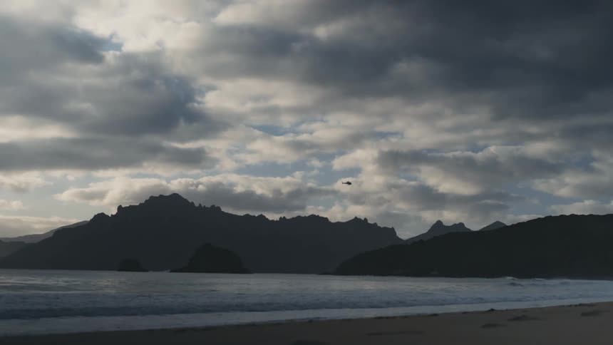 A helicopter flies over the mountains on the shore