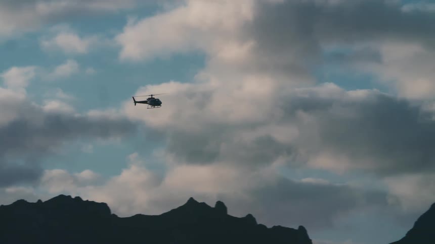 A helicopter flies over a rough rocky mountain
