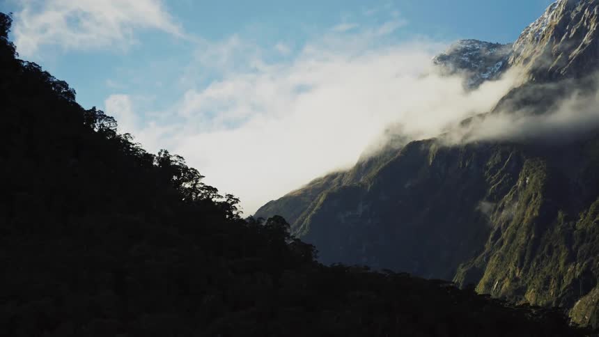 A mountain full of trees and vegetation and another is partially covered by a cloud