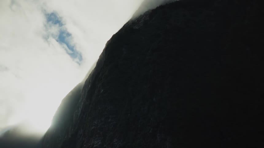 Sun rays beam from behind a mountain peak with clouds covering the tip and in the background