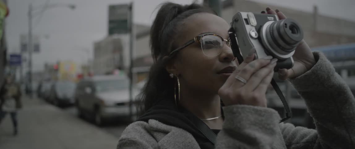 A woman walks forward on the sidewalk and takes a picture