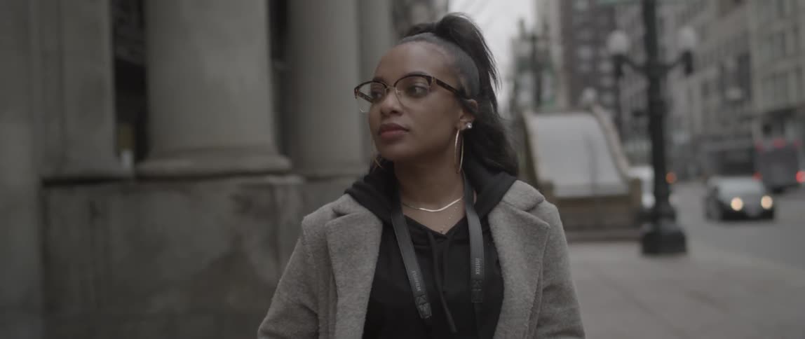 A woman is walking down the sidewalk of a city on a cloudy day