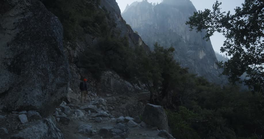 Man hiking on a rocky terrain along the slope of a cliff in a forested area
