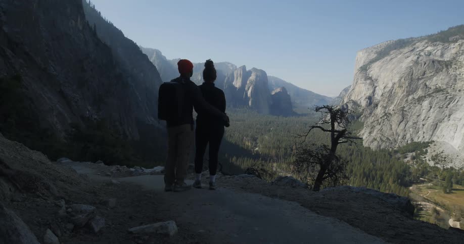 Couple facing away observing the view of a landscape with mountains and peaks in the daylight
