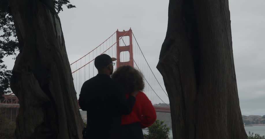 Tender moment between a man and a woman framed by two trees as they admire the golden gate bridge