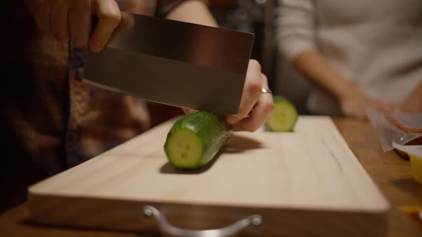Man cutting a cucumber on a wooden cutting board in the kitchen