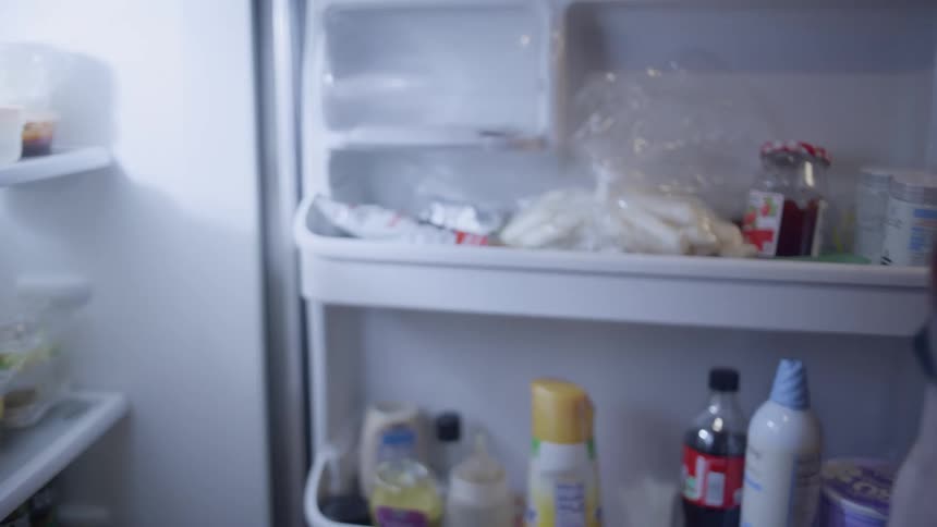 Man crouching down and grabbing vegetables from the refrigerator