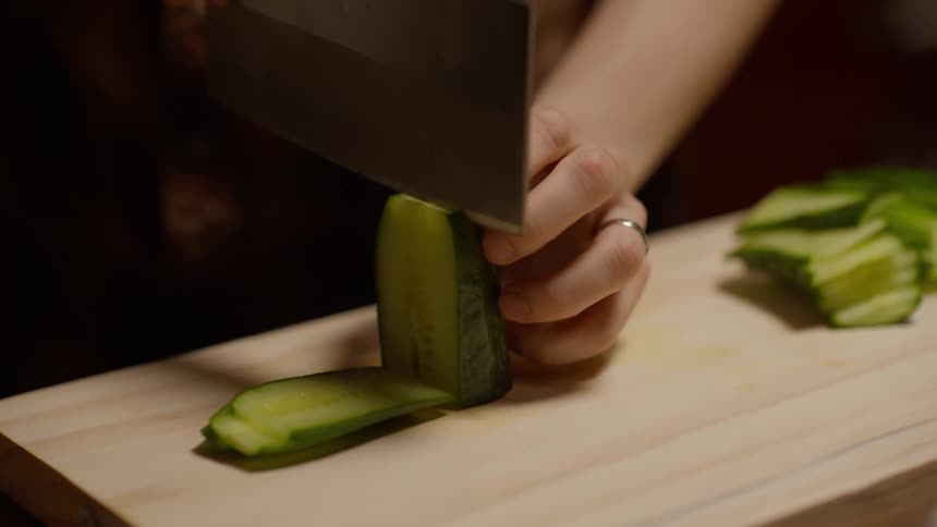 A person carefully cutting a cucumber on a wooden cutting board