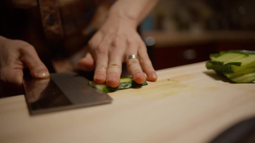 Man skillfully slicing a cucumber on a wooden cutting board