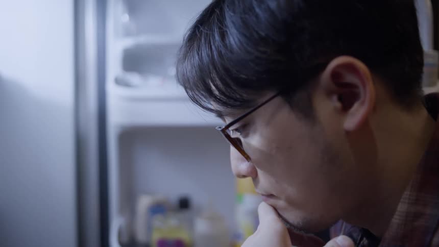 A man looks for something in a refrigerator then closes it without finding it